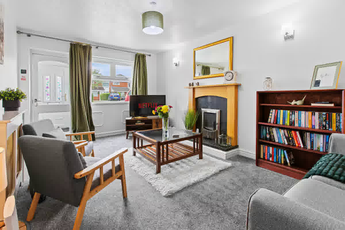 Bright living room with green curtains, a wooden fireplace, bookshelves and a smart TV — The Elton, a Gales-managed contractor let near Stanlow