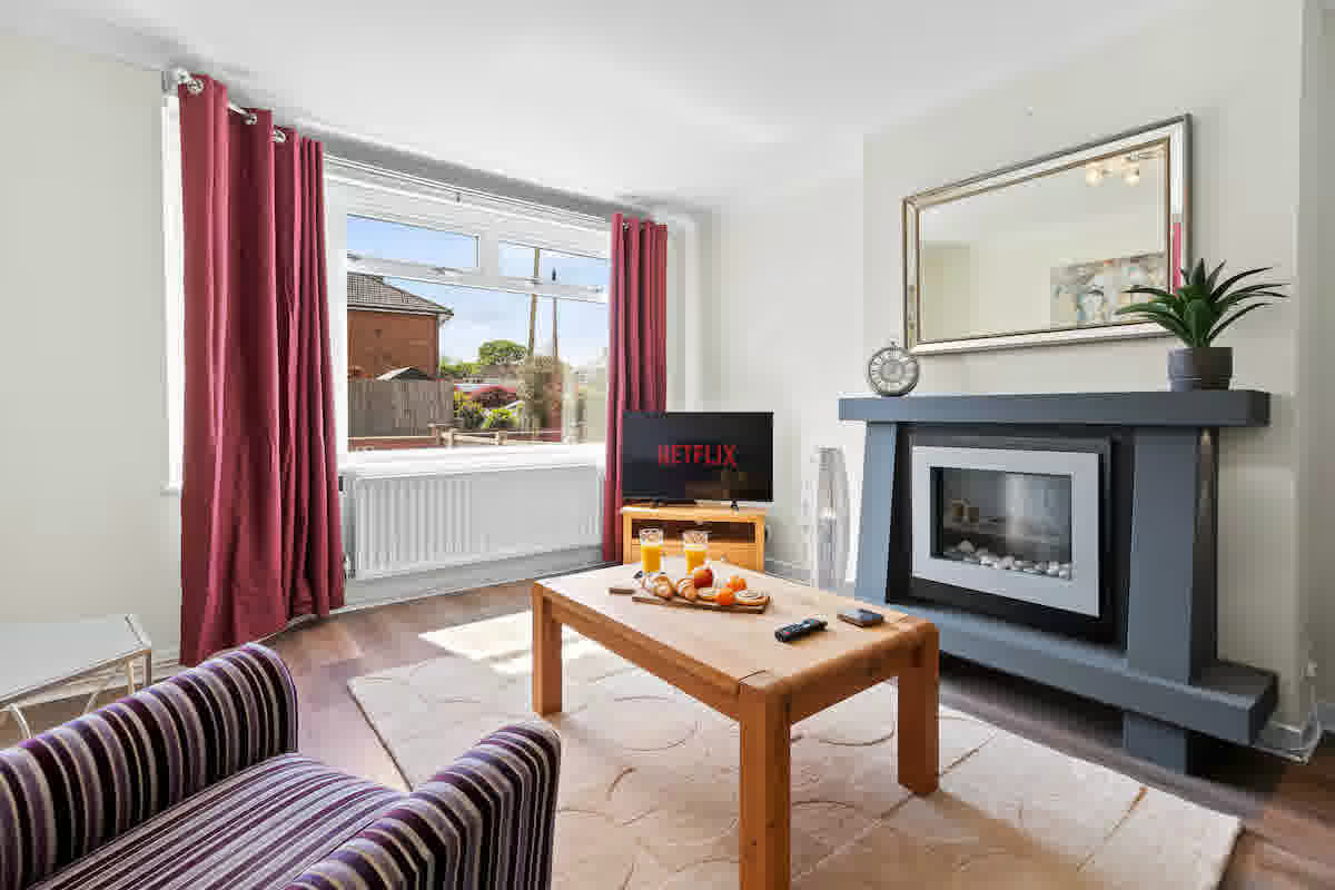 Bright living room with pink curtains, a striped sofa and a blue-grey feature fireplace — The Great Sutton, a Gales-managed contractor let in Ellesmere Port